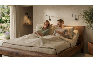 Een stel zit heerlijk in hun natuurlijke bed Beluga in massief walnoten hout van Bedaffair, de elektrische lattenbodem staat omhoog en ondersteunt hun rug zodat zij een boek kan lezen en hij een kop koffie drinkt