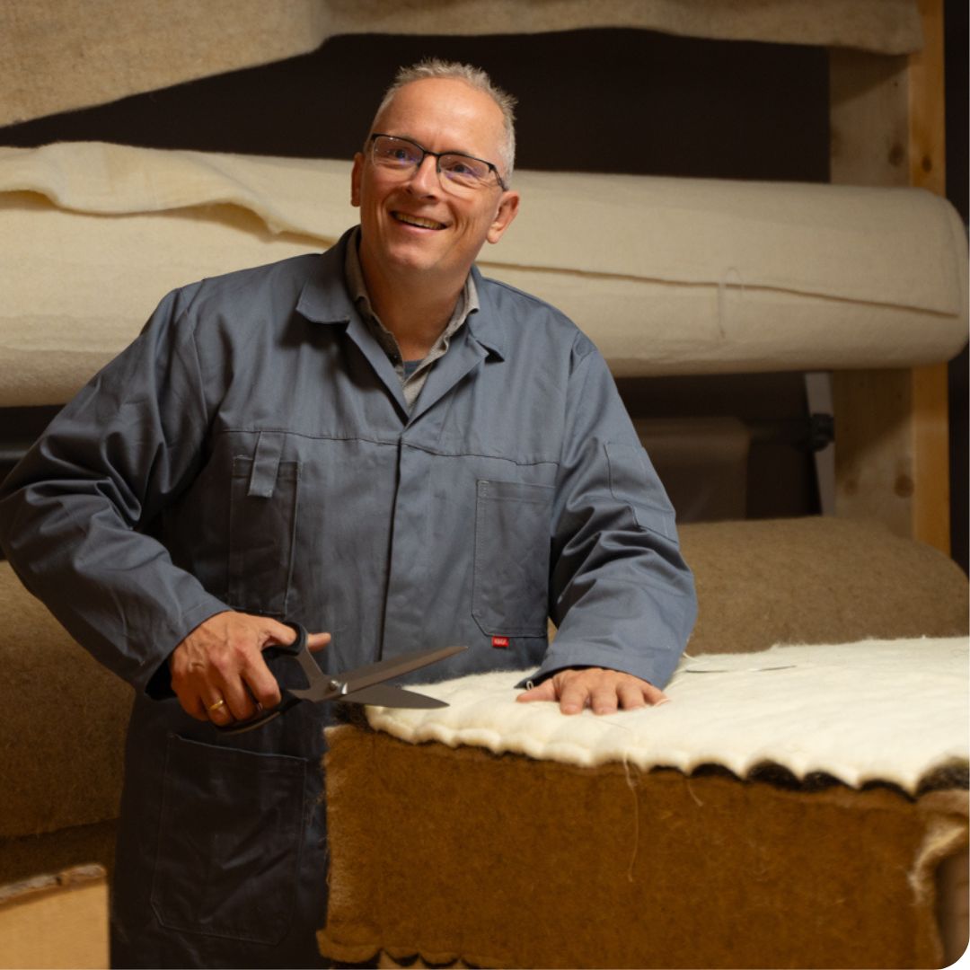 De beddenmaker van Bedaffair staat blij in de ambachtelijke productie waar hij een pocketveer matras toont met een hennep kader en een laag wol aan de bovenkant.